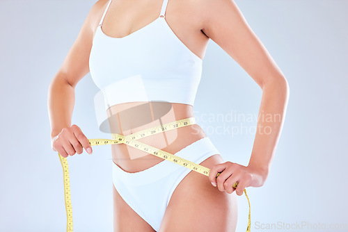 Image of Weight go away come again another day. an unrecognisable woman standing alone measuring tape around her waist against a white background.