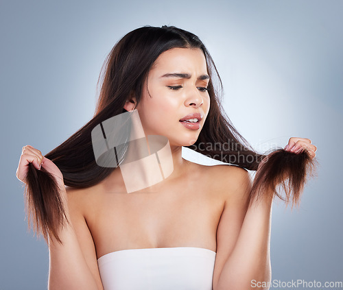 Image of Young mixed race woman holding her long brown hair and looking at damaged split ends. Woman looking upset about hair care problems