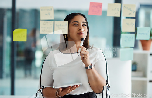 Image of Thinking carefully about all her big ideas. a young businesswoman using a digital tablet while brainstorming with notes on a glass wall in an office.