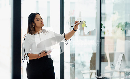 Image of Formulating new ideas with the help of her smartest tool. a young businesswoman using a digital tablet while brainstorming with notes on a glass wall in an office.