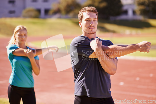 Image of Focussed on the race. two young people stretching on a athletics track.