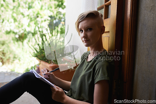 Image of Shes getting her ideas down. Portrait of an attractive young woman sitting outside on the porch writing in a notepad.