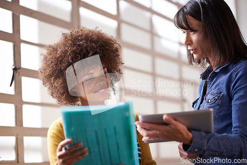 Image of Making some last minute changes. two female colleagues having a discussion while standing with a digital tablet and documents.