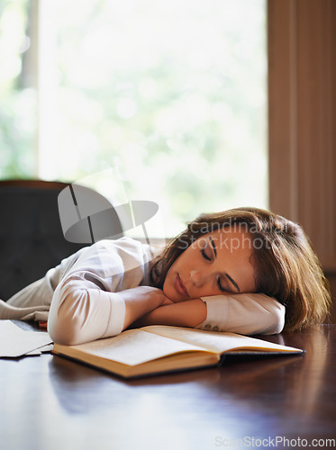 Image of She got lost somewhere in between the pages. an attractive young woman enjoying a peaceful nap at home with a book in front of her.