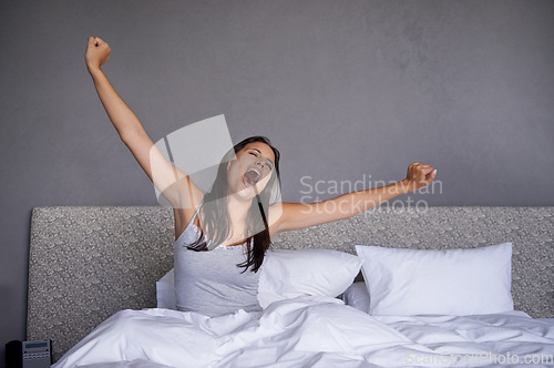 Image of Time to get up. a young woman yawning while stretching in bed.