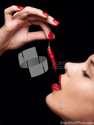 Image of Lets see if this will make me any hotter. Studio shot of a beautiful young woman bringing a chili to her lips.
