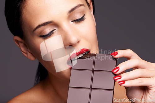 Image of Every woman needs a guilt-free chocolate day. Closeup portrait of a cute young female biting into a piece of chocolate.