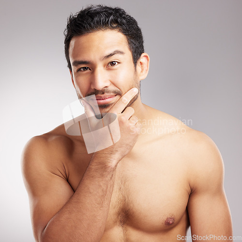 Image of Handsome young mixed race man touching his face and posing shirtless isolated in studio against a grey background. Hispanic well groomed male looking confident and happy with his daily skincare regim