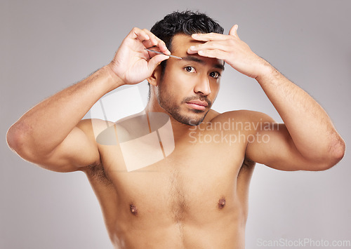 Image of Handsome young mixed race man posing shirtless in studio isolated against a grey background. Hispanic male plucking his eyebrows with a tweezers. All part of his daily grooming and skincare routine