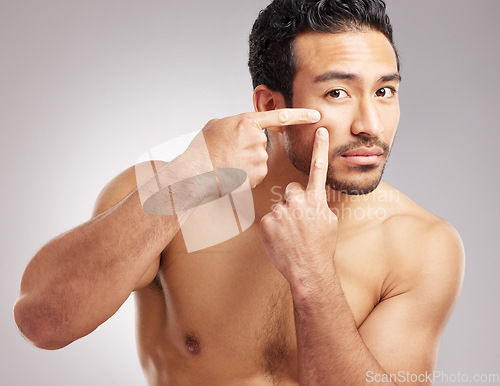 Image of Handsome young mixed race man posing shirtless in studio isolated against a grey background. Hispanic male popping pimples or zits on his face. No outbreaks in the plans for his skincare regime