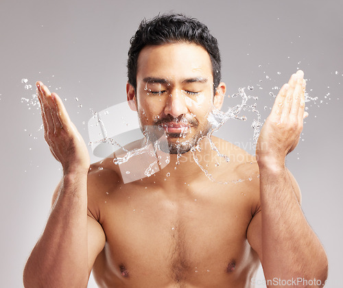 Image of Handsome young mixed race man shirtless in studio isolated against a grey background. Hispanic male washing his face with water. Rinsing off his skin to keep it clean and hygienic as part of skincare