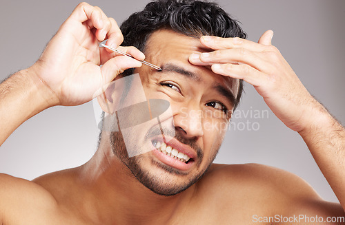 Image of Handsome young mixed race man shirtless in studio isolated against a grey background. Hispanic male wincing in pain while plucking his eyebrows with a tweezers. Part of his daily grooming routine