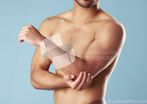 Image of Closeup young mixed race man standing shirtless in studio isolated against a blue background. Unrecognizable topless male athlete suffering from an arm or elbow injury. Muscle cramp, ache or pain