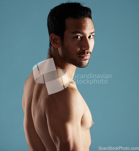 Image of Handsome young hispanic man standing shirtless in studio isolated against a blue background. Mixed race topless male athlete looking confident, healthy and fit. Exercising to increase his strength