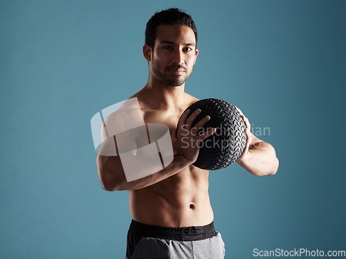 Image of Handsome young hispanic man training with a medicine ball in studio isolated against a blue background. Mixed race shirtless male athlete exercising or working out to increase his strength and fitnes