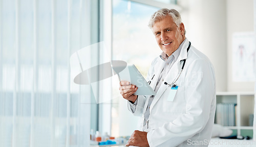 Image of Happy mature male doctor holding a digital tablet. Smiling senior practitioner using digital tablet to check medical records or results in a hospital