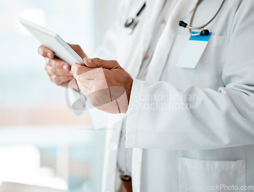 Image of Closeup of expert male doctor holding and using a digital tablet, working at a hospital alone. One caucasian man wearing a labcoat working on a digital tablet standing in an office at a clinic