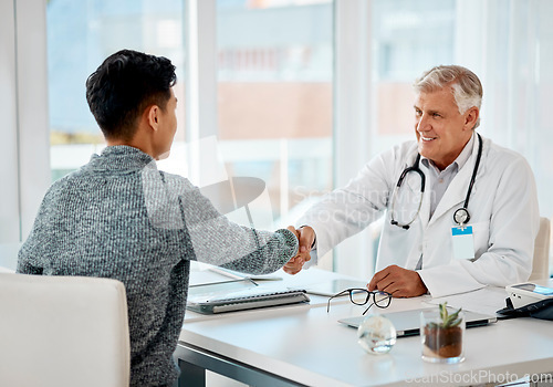 Image of Mature caucasian doctor greeting a patient with a handshake for a consultation. Senior medical professional smiling in meeting with a patient at the hospital. Two men greeting during a consult