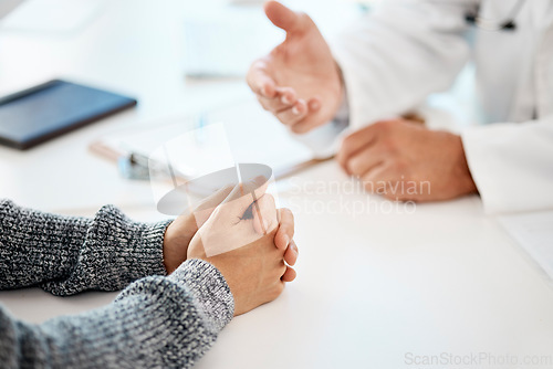 Image of Above closeup of hands during a consult between a caucasian man doctor and male patient at a table in the clinic. Mixed race patient with clasped hands receiving advice from his doctor about medical