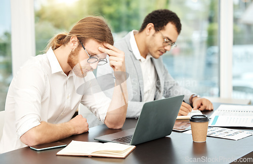 Image of I just cant focus today. a young businessman looking stressed out while working on a laptop in an office with his colleague in the background.