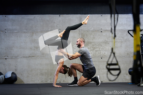 Image of A muscular man assisting a fit woman in a modern gym as they engage in various body exercises and muscle stretches, showcasing their dedication to fitness and benefiting from teamwork and support