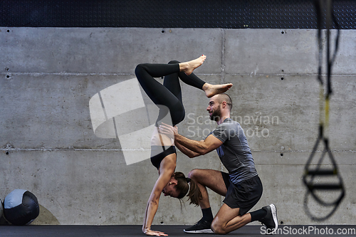 Image of A muscular man assisting a fit woman in a modern gym as they engage in various body exercises and muscle stretches, showcasing their dedication to fitness and benefiting from teamwork and support