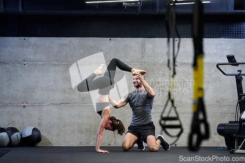 Image of A muscular man assisting a fit woman in a modern gym as they engage in various body exercises and muscle stretches, showcasing their dedication to fitness and benefiting from teamwork and support