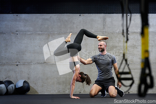 Image of A muscular man assisting a fit woman in a modern gym as they engage in various body exercises and muscle stretches, showcasing their dedication to fitness and benefiting from teamwork and support