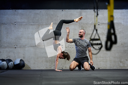 Image of A muscular man assisting a fit woman in a modern gym as they engage in various body exercises and muscle stretches, showcasing their dedication to fitness and benefiting from teamwork and support