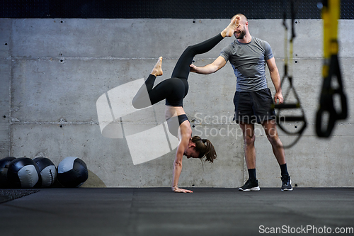 Image of A muscular man assisting a fit woman in a modern gym as they engage in various body exercises and muscle stretches, showcasing their dedication to fitness and benefiting from teamwork and support