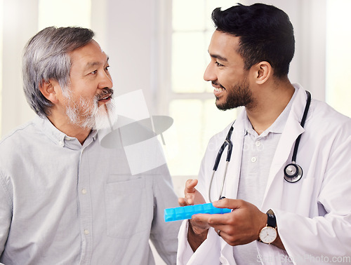Image of Keep them organised and take them daily. a doctor holding a pill box while talking to a senior patient.