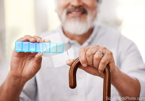 Image of This helps me to remember what medication to take. a senior man sitting with a walking stick and holding up a weekly pill box.