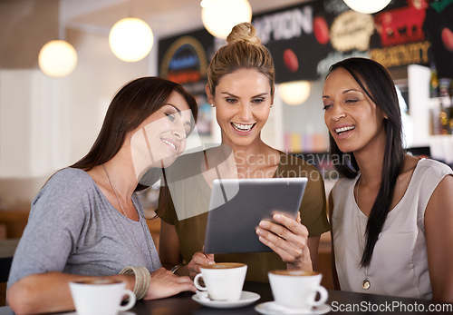 Image of Walking down memory lane with the girls. Three attractive young women gathered around a tablet pc in a restaurant.