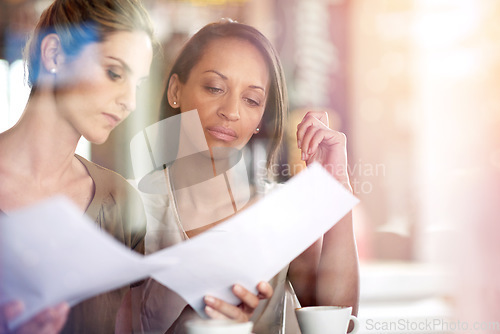 Image of Getting down to business with coffee. Two women discussing paperwork during a business meeting at a cafe.