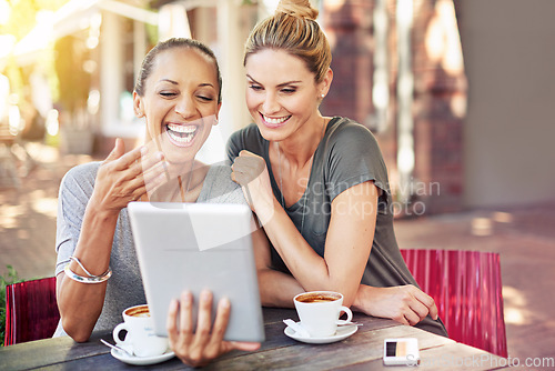 Image of Thats so funny. two women sitting with a tablet at a coffee shop.