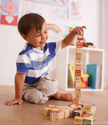 Image of Make the tower bigger. A young boy playing with his building blocks in his room.