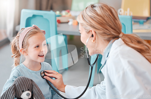 Image of Young caucasian female doctor doing a checkup on a happy and cheerful little at a hospital. Carefree little girl smiling while holding a toy during a medical exam at daycare.