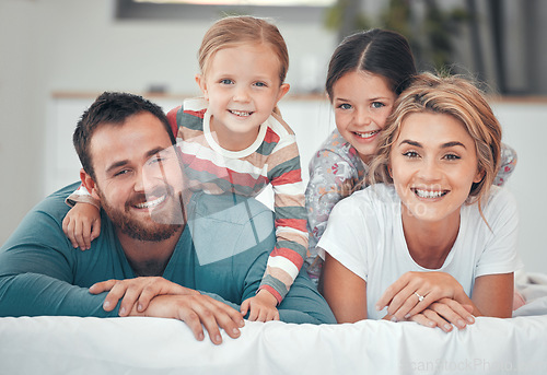 Image of Happy caucasian family of four in pyjamas cosy together in bed at home. Two little kids lying on top of their loving parents. Adorable playful young girls bonding with their mom and dad during bedtim