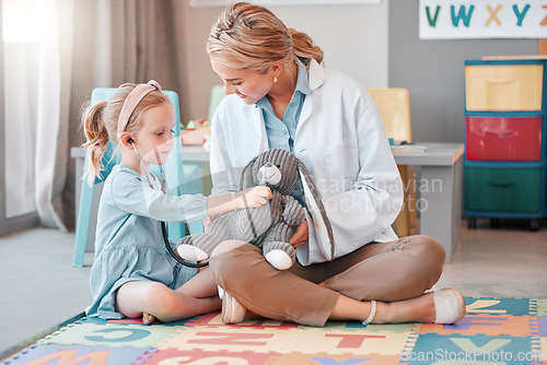 Image of Young caucasian paediatrician helping a little girl listen to the heartbeat of a toy with a stethoscope, Small, happy child visiting the doctor for a checkup, playing on the floor together.