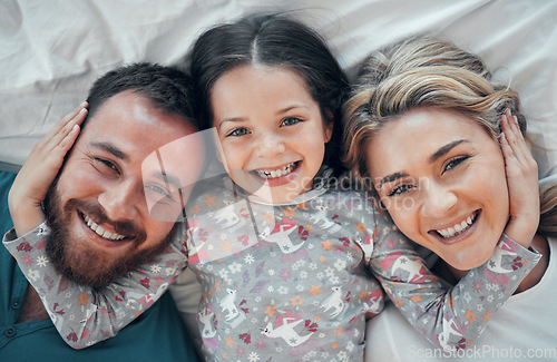 Image of Happy carefree caucasian family in pyjamas from above lying cosy together in bed at home. Loving parents with their little daughter. Adorable young girl hugging her mom and dads face during bedtime