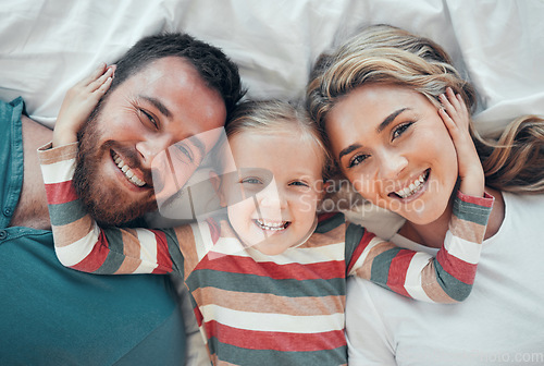 Image of Happy smiling caucasian family of three looking cosy together in bed at home. Loving parents with their little daughter. Adorable young girl hugging her mom and dads face and taking a selfie