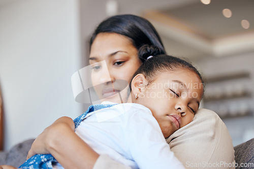 Image of Young mixed race mother looking worried while holding her daughter while she sleeps and sitting on the couch in the lounge at home. Little girl looking comfy while sleeping and hugging her mom