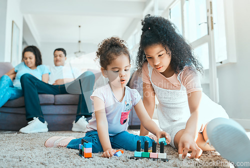 Image of Tell them to keep the dolls. two sister playing on the floor while their parents relax in the background.