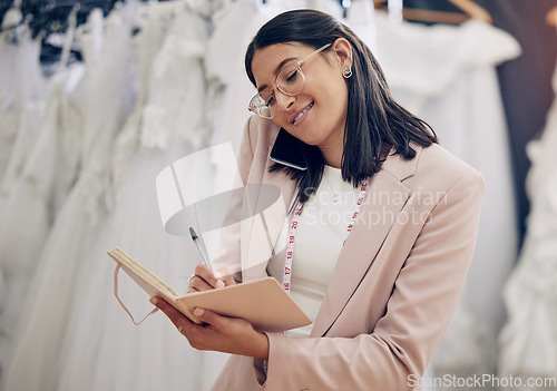 Image of Ill put you down for a fitting. an attractive young seamstress writing notes while talking on her cellphone.