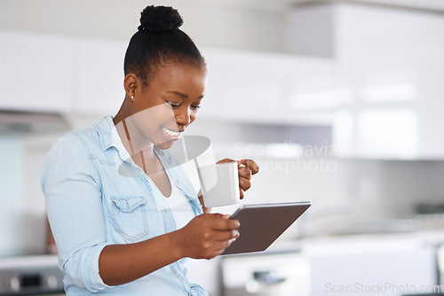 Image of I love that technology keeps me in the know. a woman drinking coffee while using a digital tablet at home.