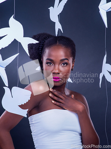 Image of Beauty is a radiance that originates from within. Studio portrait of a beautiful young woman posing with paper birds against a black background.
