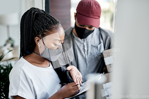 Image of Handled with the care your package deserves. a masked young woman signing for a delivery received at home.