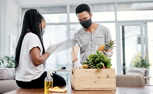 Image of Making sure their order is in order. a masked young couple using a digital tablet while disinfecting their groceries at home.