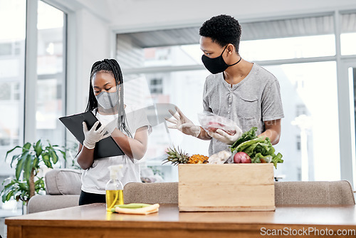 Image of When unpacking groceries turns into a production line. a masked young couple disinfecting their groceries at home.