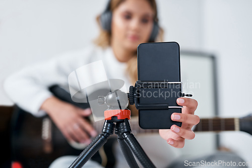 Image of I use my music to express myself. a young woman using her cellphone to record herself while playing the guitar at home.